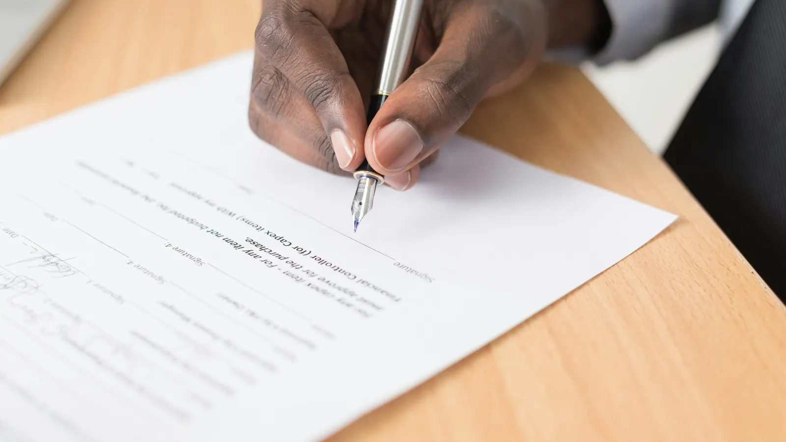 Close-up of a hand signing a printed form with a fountain pen on a wooden desk