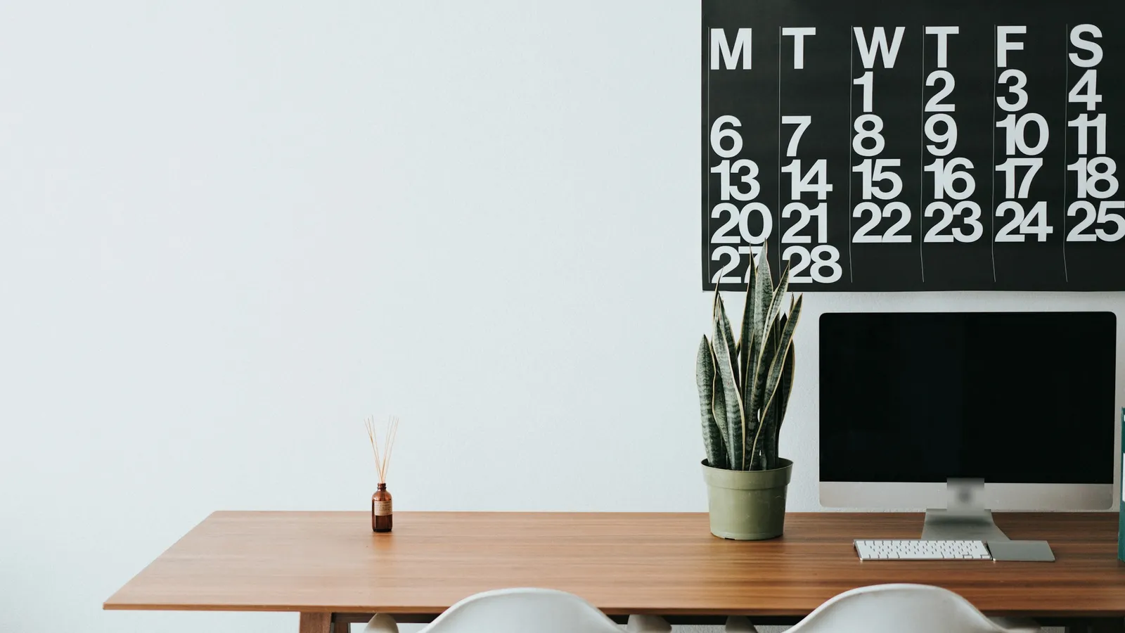 Large monthly wall calendar above a wooden desk with a desktop computer and a plant