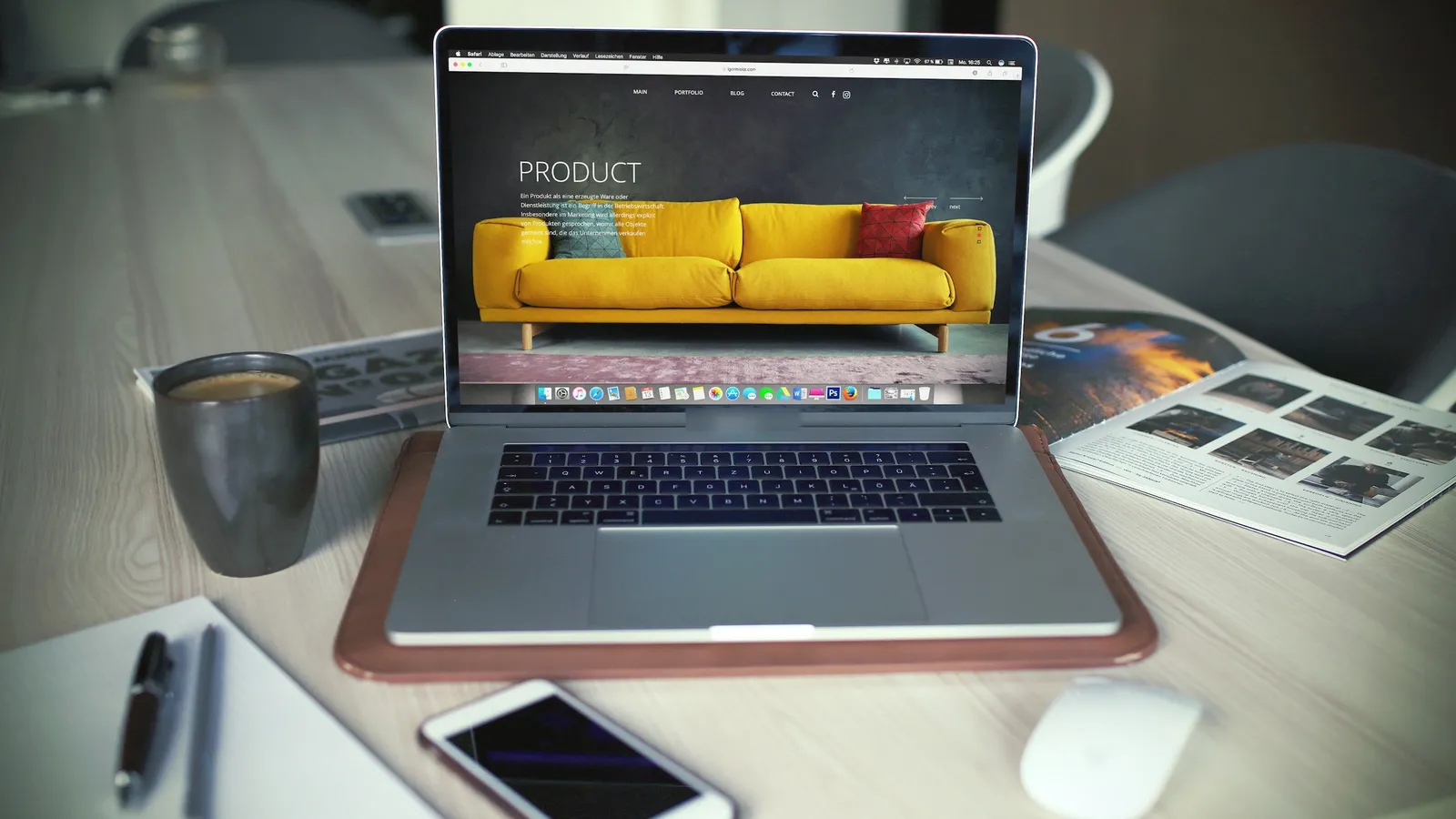 Laptop showing an online store product page with a yellow sofa, beside a coffee mug and a phone