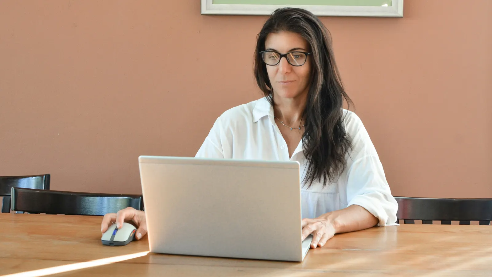 Woman in glasses working on a laptop at a wooden table