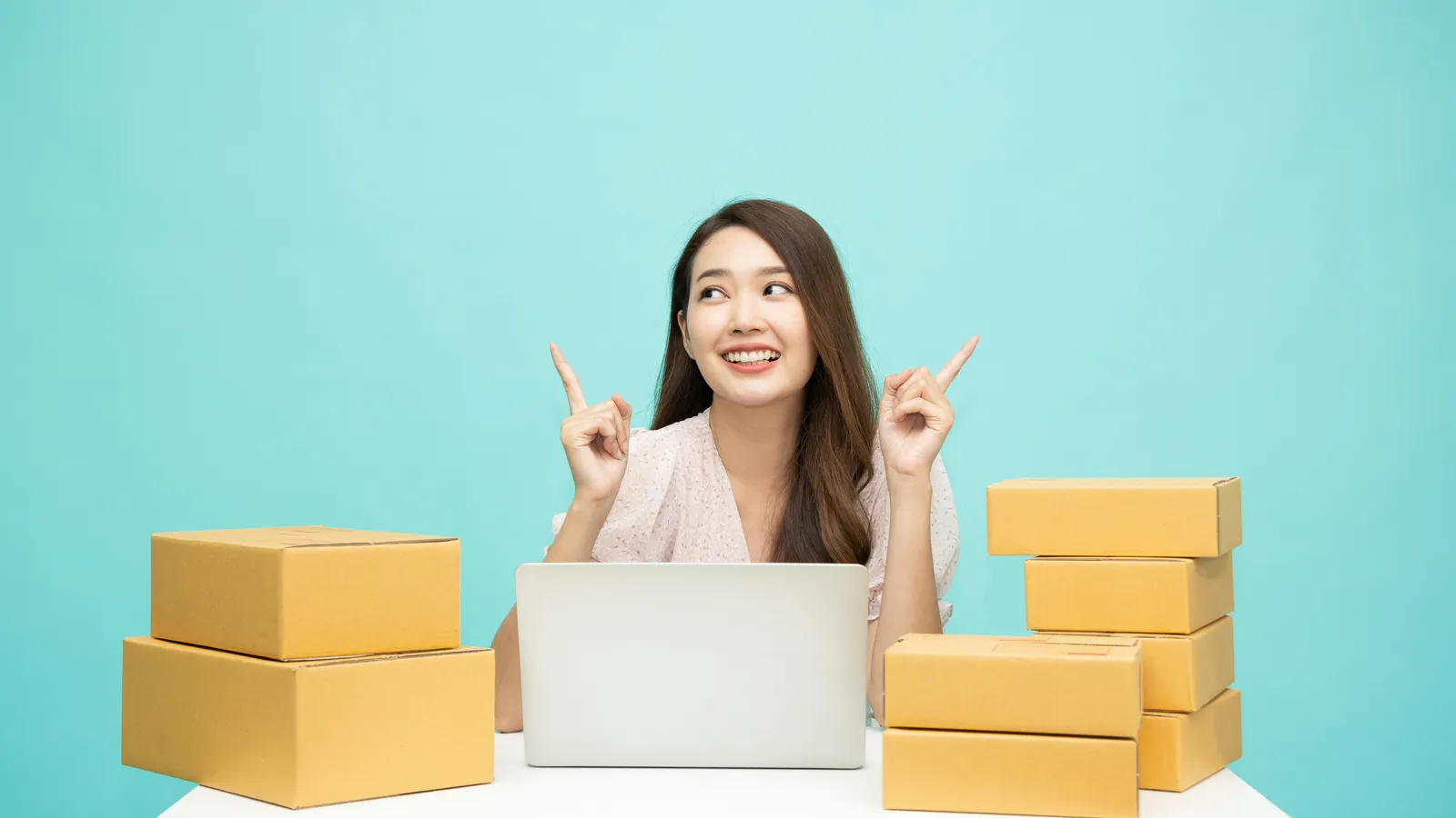 Smiling small business owner at a laptop between stacks of shipping boxes