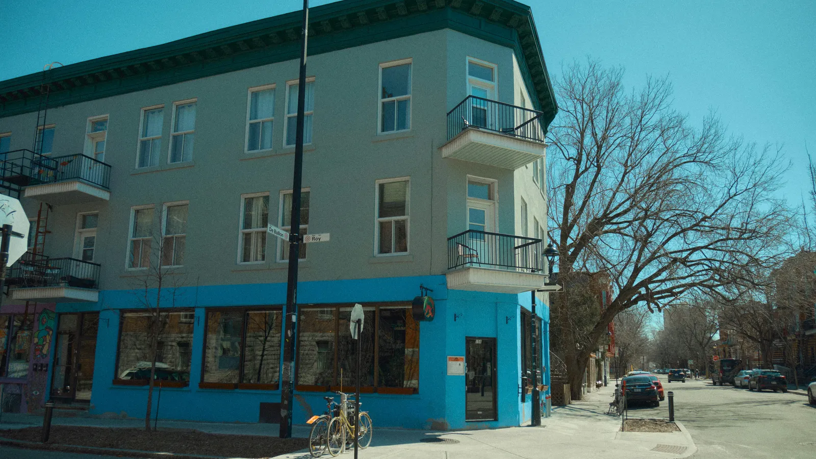 Corner building with a bright blue ground-floor storefront on a quiet tree-lined street