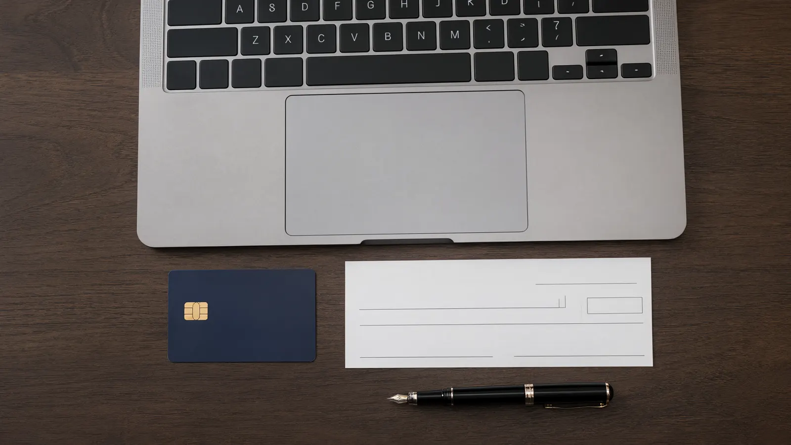 Overhead view of a laptop above a plain dark blue chip card, a blank check and a fountain pen on a dark wood desk