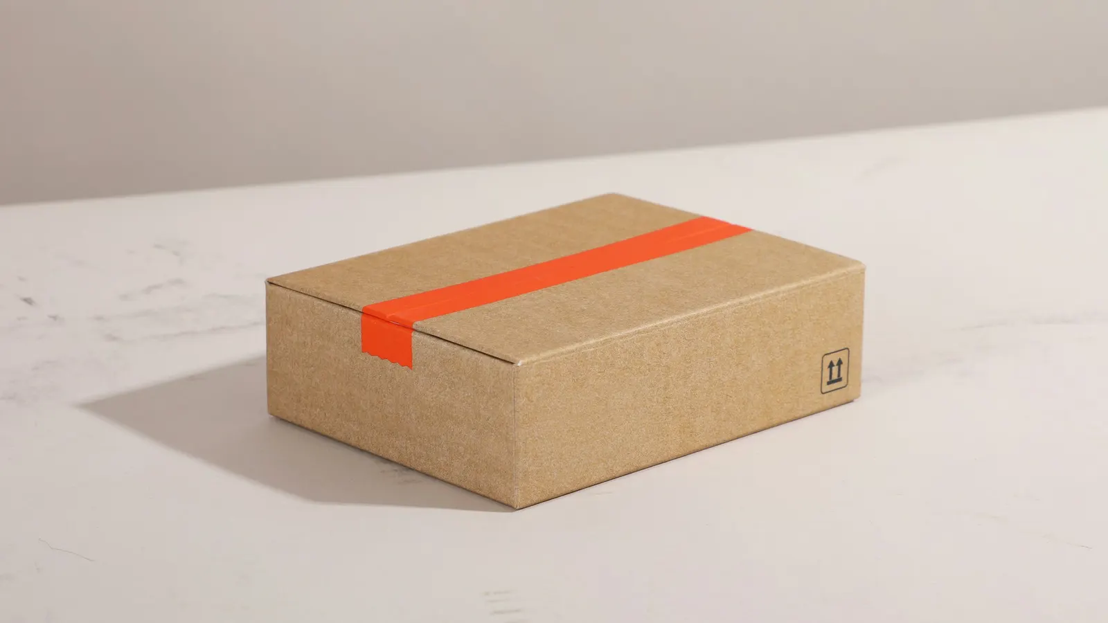 Closed cardboard shipping box sealed with orange tape on a white surface