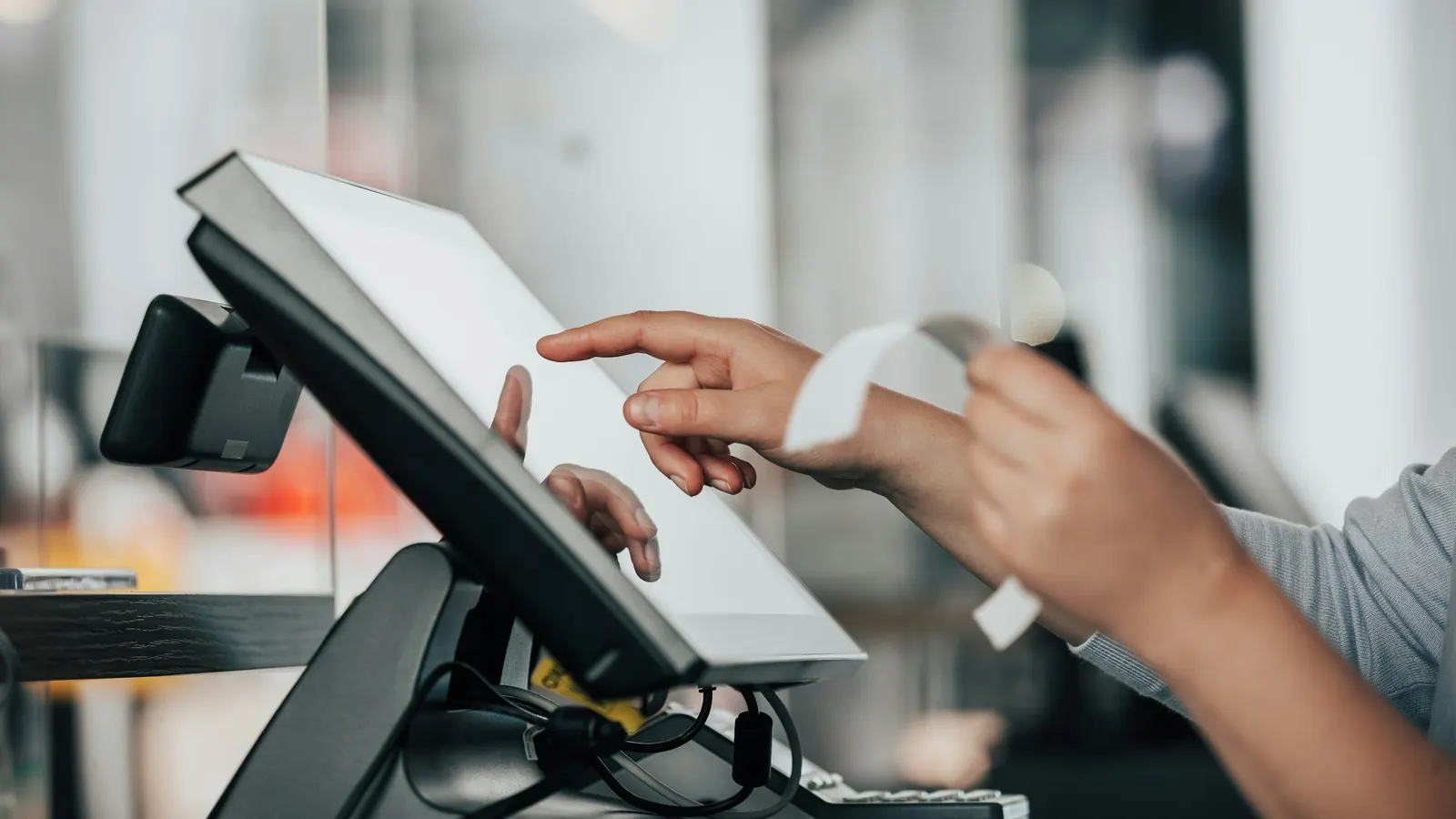 Cashier using a touchscreen POS terminal and handing over a card receipt at checkout