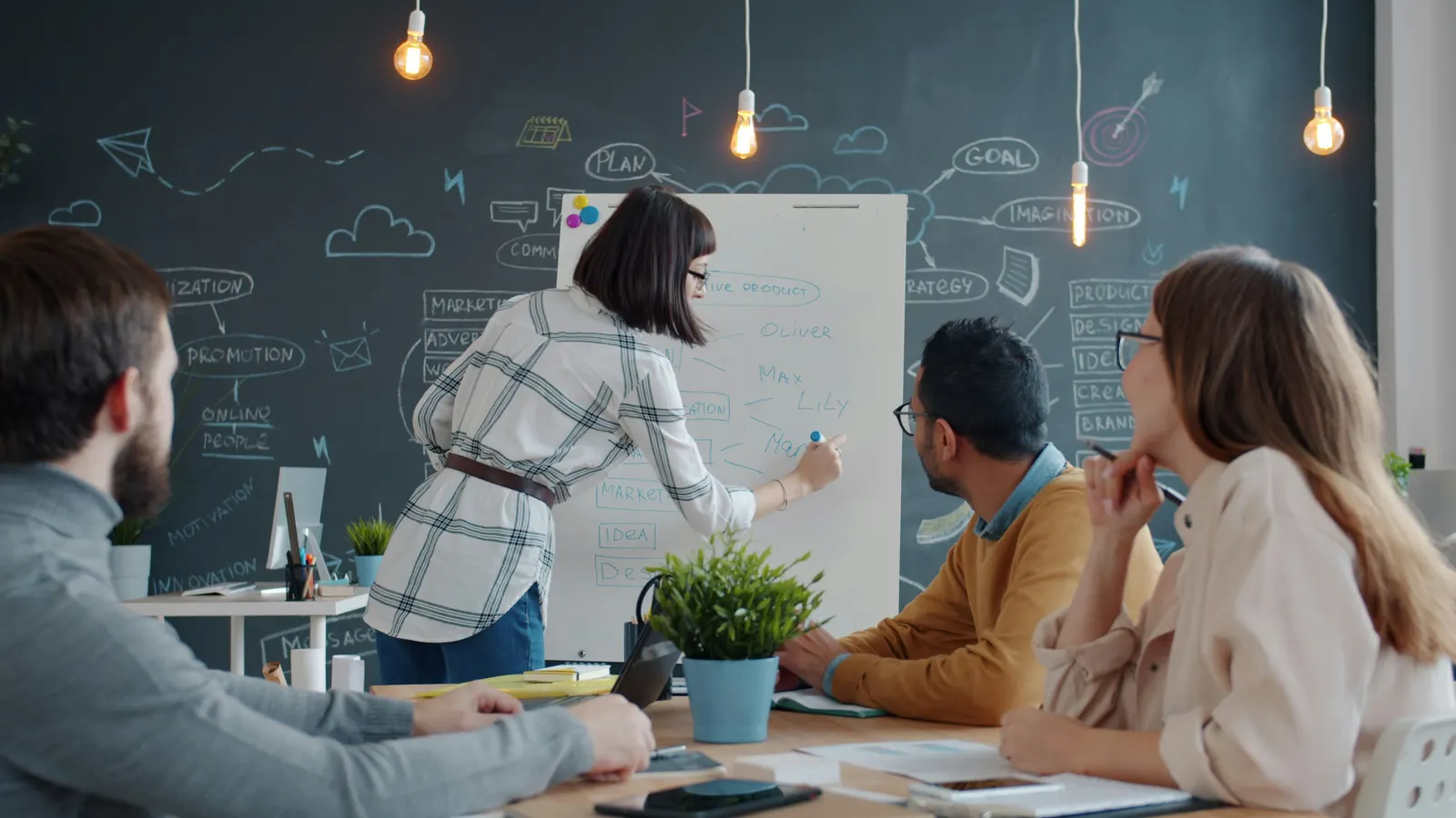 Woman writing on a flip chart while three colleagues watch from a meeting table