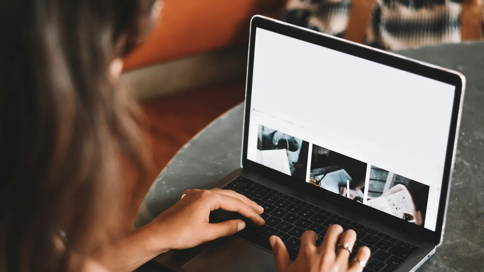 Woman typing on a laptop that shows a web page with a row of photos