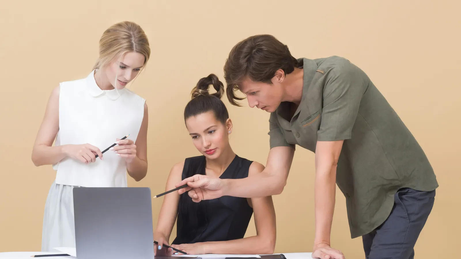 Man pointing at a laptop screen while explaining something to two women