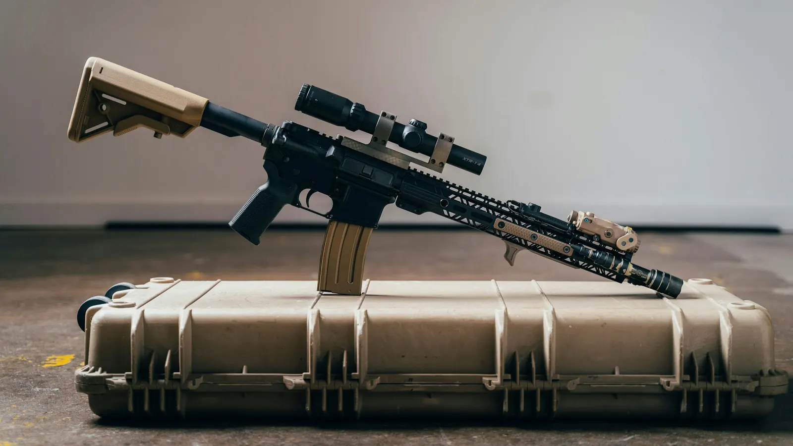 AR-style rifle with a scope resting on a tan hard-sided rifle case