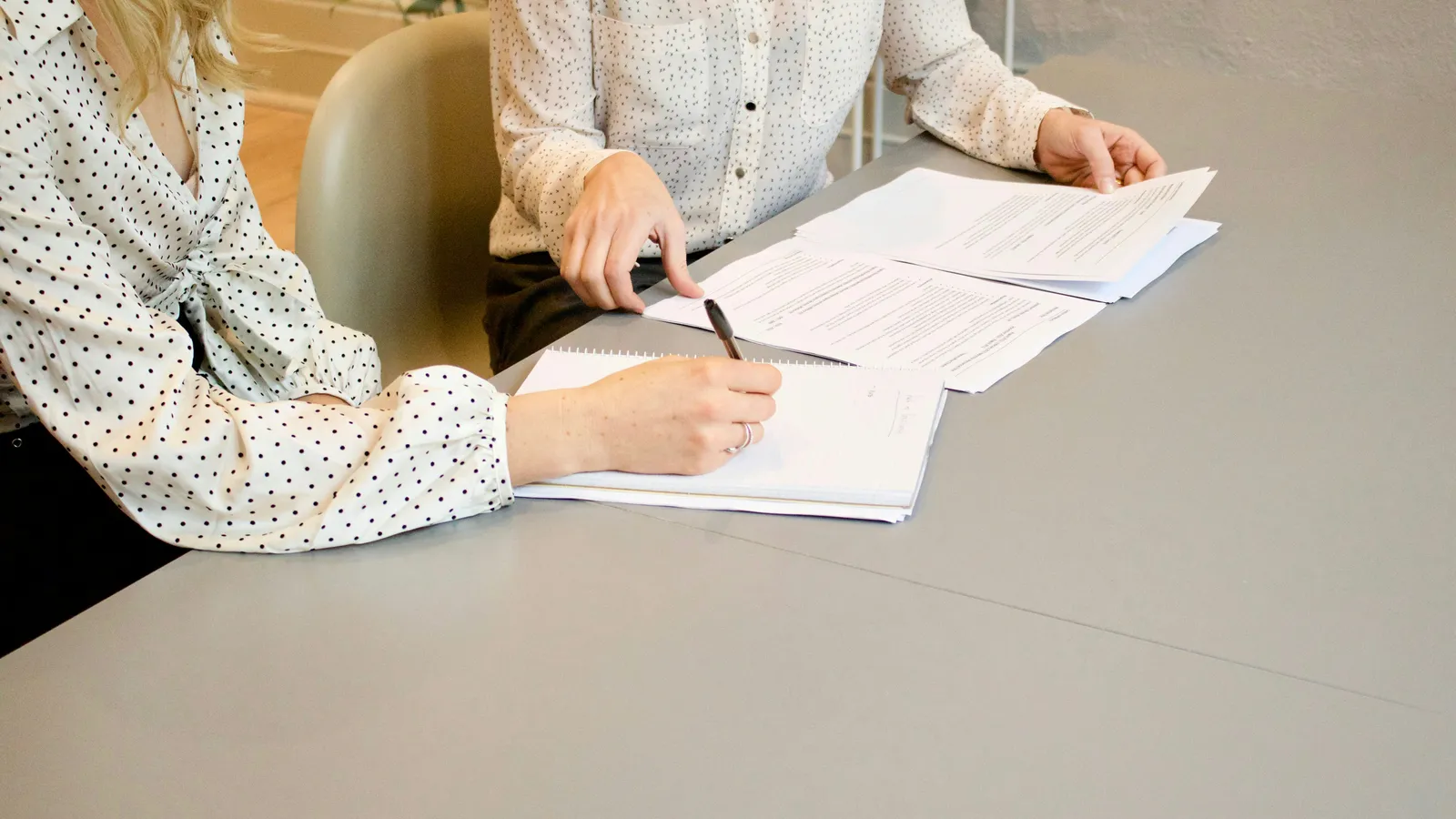 Two people at a table reviewing printed documents while one signs with a pen