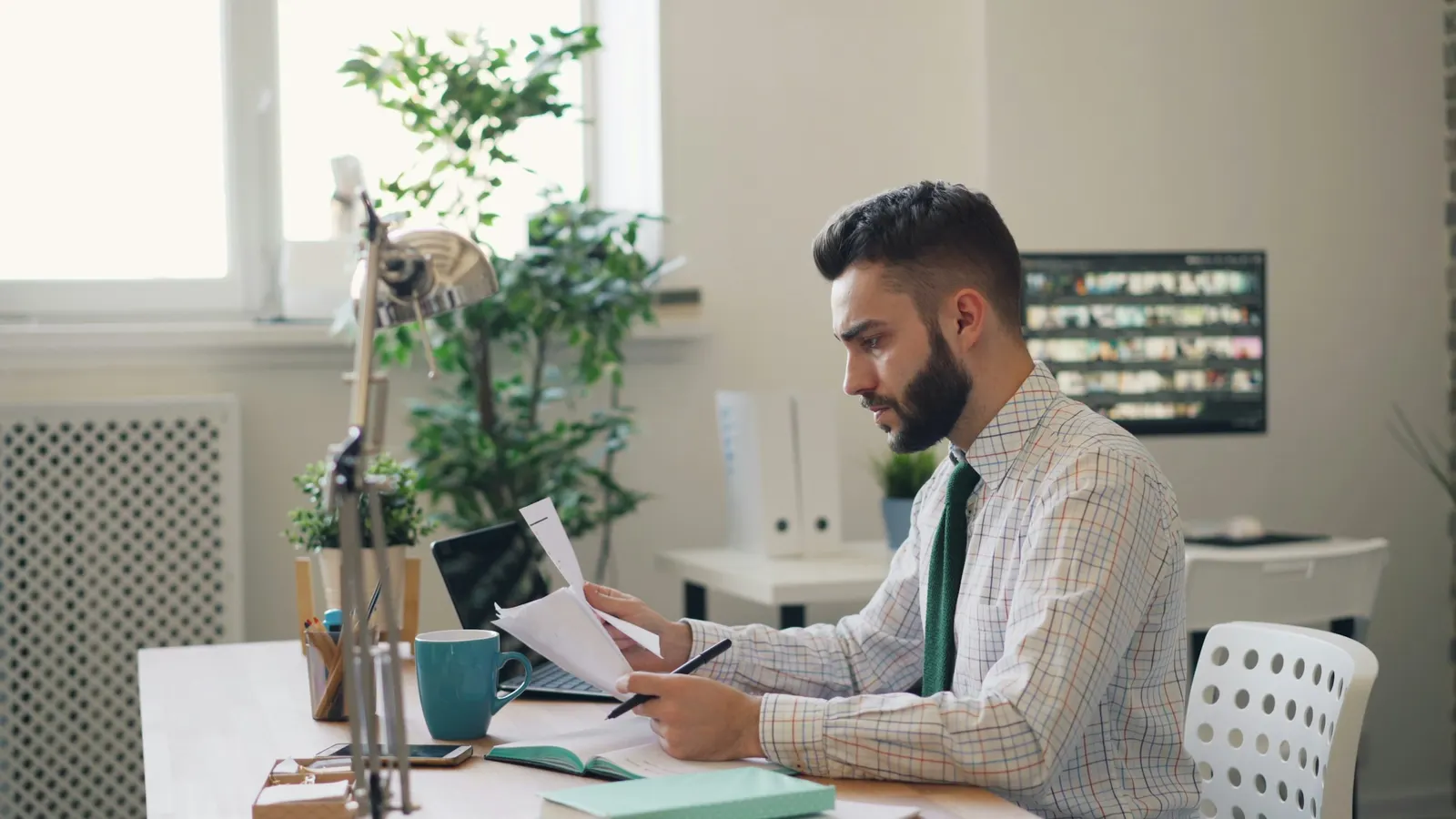 Business owner reviewing paperwork with a pen at a desk beside an open laptop