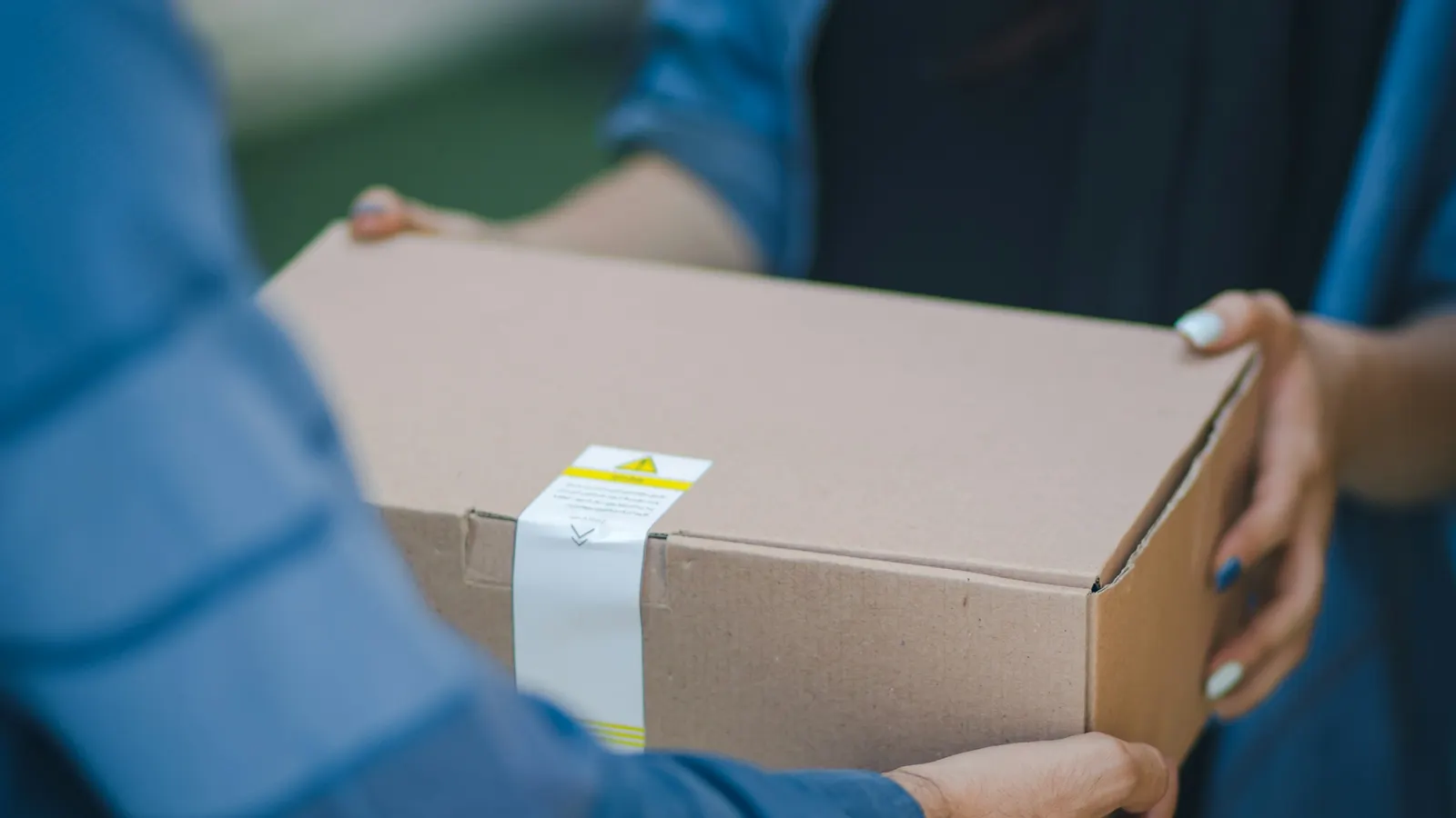 One person handing a taped cardboard package to another person